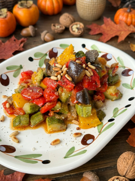 Caponata di ottobre con melanzane, zucchine, peperoni e pomodorini al forno, completata con capperi, pinoli tostati ed erbette aromatiche.