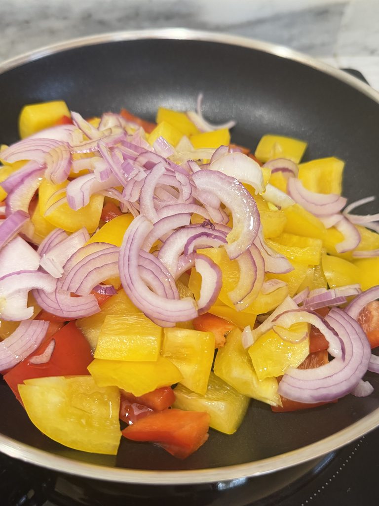Cipolla rossa di Tropea a fette spesse e peperoni a pezzi in padella durante la preparazione della caponata di ottobre