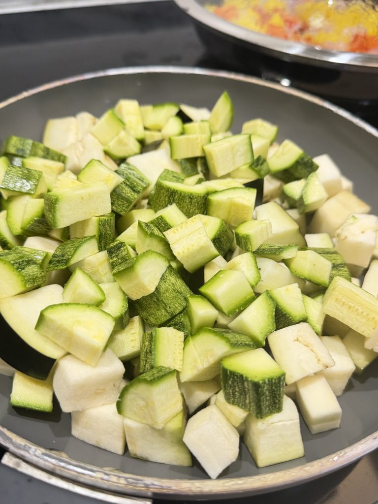 Zucchine e melanzane a cubetti in cottura in una padella antiaderente per la caponata di ottobre.